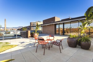 Una terraza en la azotea con mobiliario exterior, plantas en macetas y vistas de la ciudad.