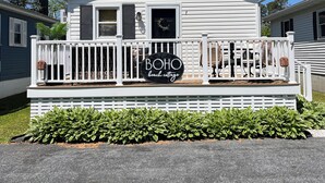 Une maison mobile blanche avec un porche, une enseigne indiquant « maison de plage de style bohème » et une guirlande sur la porte.