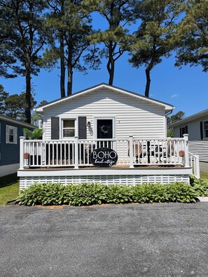 A white mobile home with a porch, a sign reading 'BOHO beach cottage,' and a wreath on the door.