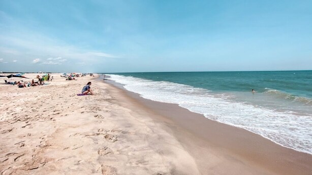 Une plage avec un ciel dégagé, une eau calme et des gens qui se détendent sur le sable.