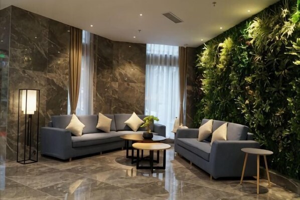 Een moderne lobby met twee banken, een vloerlamp, een bijzettafeltje en een groene wand.