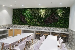 Une salle de conférence avec des tables et des chaises blanches, un mur vert orné de plantes et un sol à motifs.