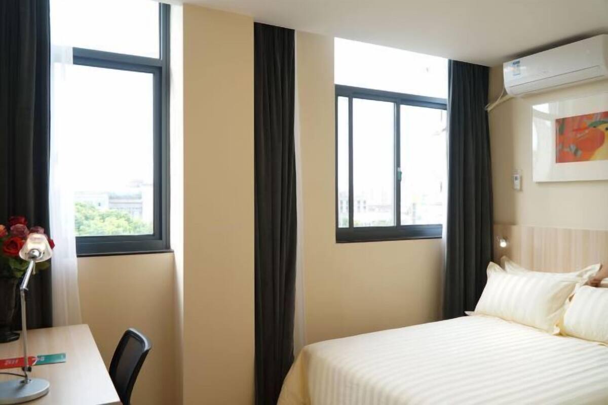 Une chambre d’hôtel avec un lit, un bureau, une lampe et une fenêtre avec des rideaux.