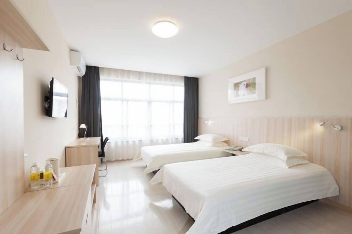 Une chambre d’hôtel avec deux lits, un bureau, une chaise, un téléviseur à écran plat et une fenêtre avec des rideaux.