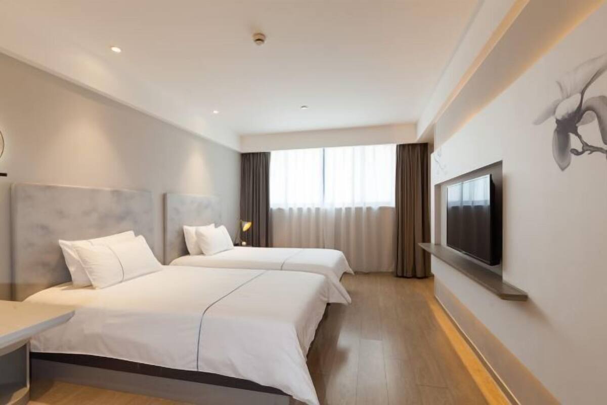 Une chambre d’hôtel moderne avec deux lits, un téléviseur à écran plat fixé au mur et une grande fenêtre avec des rideaux.