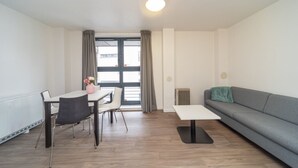 Ein modernes Wohnzimmer mit grauem Sofa, einem Esstisch mit Stühlen und einem kleinen weißen Tisch.