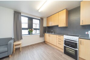 A modern kitchen with wooden cabinets, a built-in oven, and a window with curtains. - JOIVY Affordable 3,4,5 and 12 bed private flats next to Royal Mile - Adults only (Edinburgh)