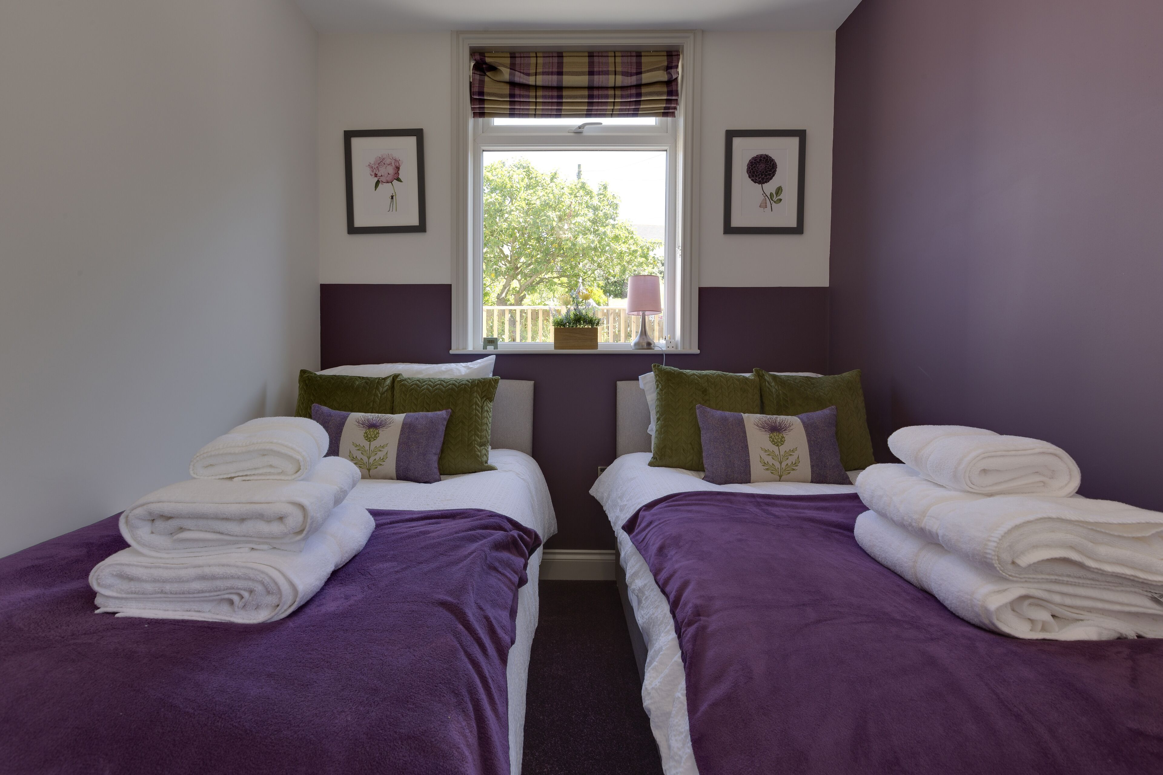A twin bedroom with two beds, purple bedding, a window with a view, and a small balcony.
