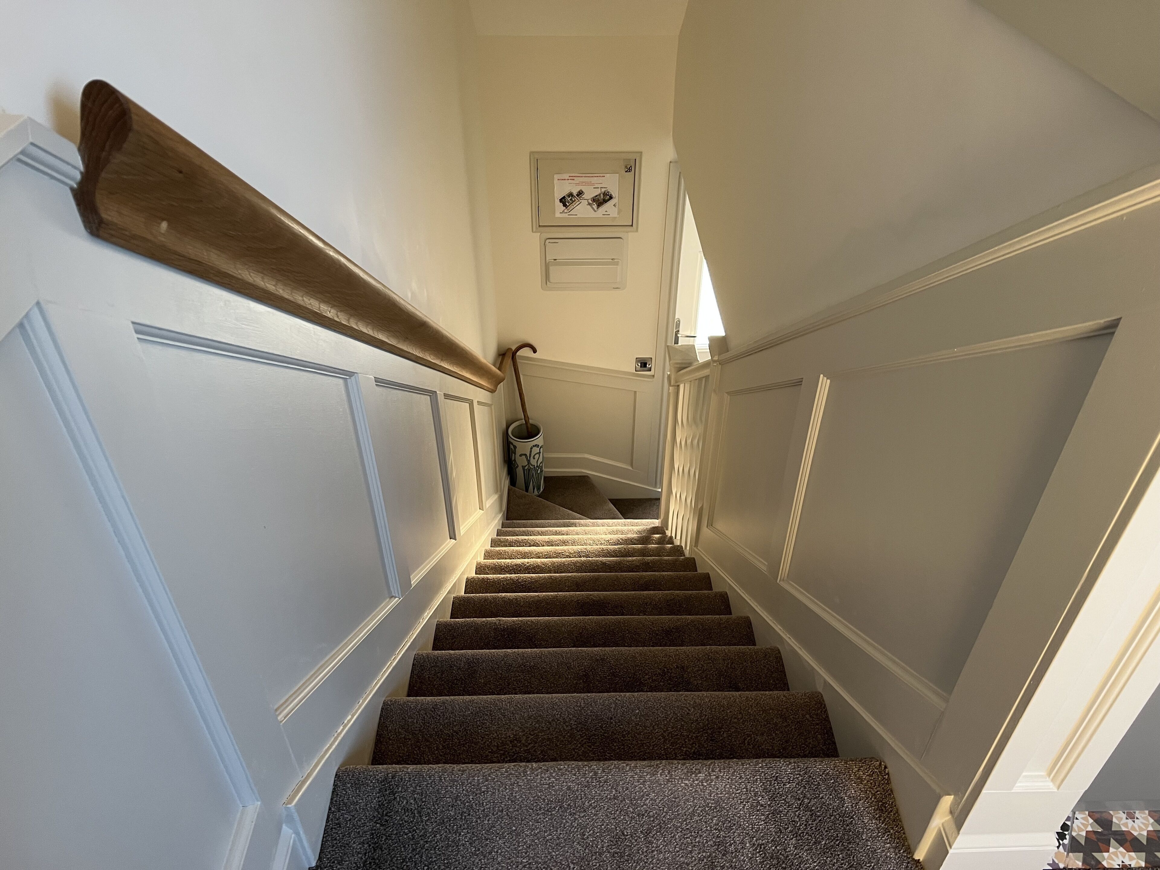 A carpeted staircase with a wooden handrail, white walls, and a light fixture above.
