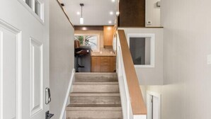 Eine Treppe mit Holzvertäfelung, weißen Wänden und einer Küche im Hintergrund.