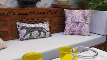 A cozy outdoor seating area with a wooden bench, two cushions, and a table with two yellow glasses and a pitcher of a beverage.
