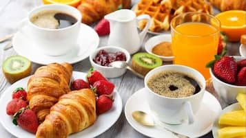 A breakfast setting with croissants, strawberries, coffee, waffles, and orange juice.