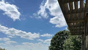 Una terraza de madera con un sendero de piedra que lleva a una zona cubierta de césped, una valla y árboles al fondo.