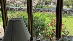 Una ventana con vistas a un jardín, una lámpara y varios jarrones de cristal en el alféizar.