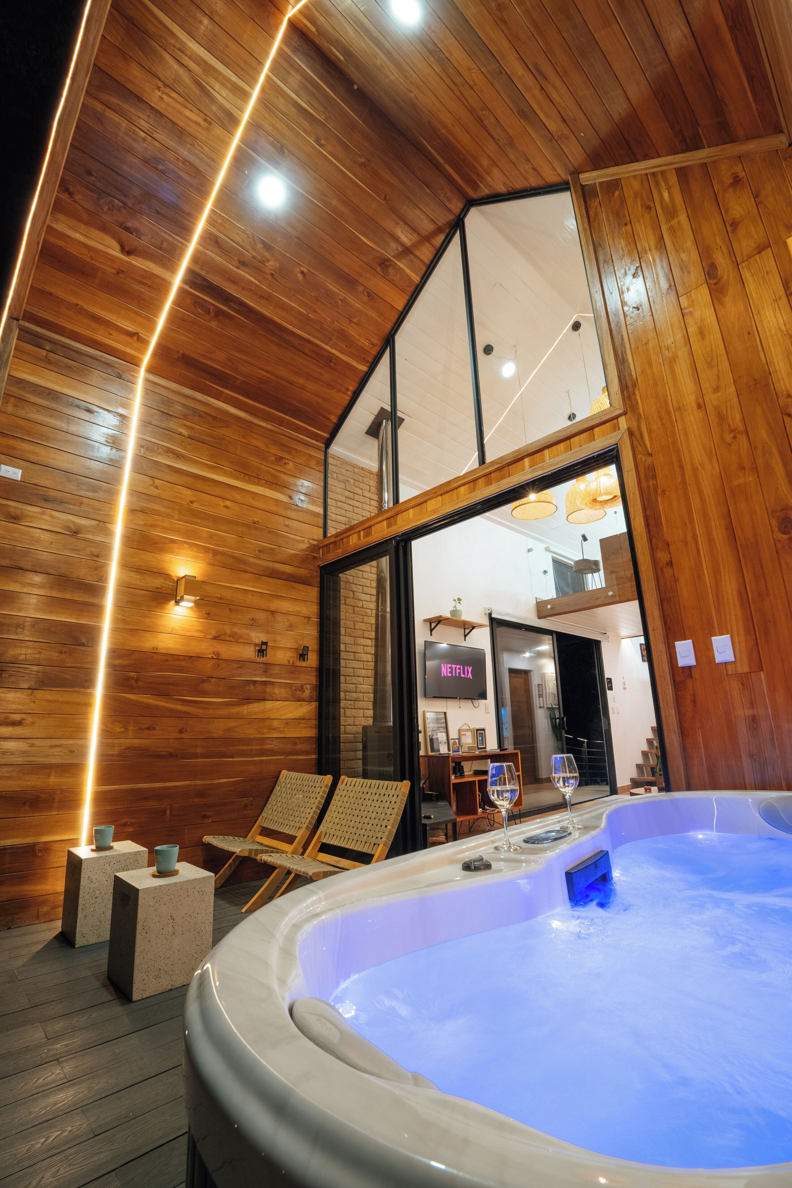 A hot tub in a wooden room with a Netflix sign, a glass door, and a lounge chair.