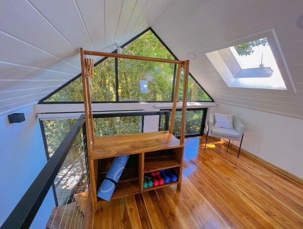 Quarto em estilo loft com cama beliche de madeira, claraboia e vista para o verde lá fora.