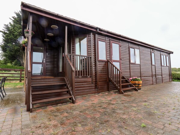 A wooden building with a porch, steps, and a flower pot. - Handale Banks Farm Lodge (Saltburn-by-the-Sea)