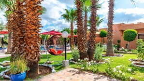 A courtyard with palm trees, a hanging chair, a pool, and a building with a unique architectural design. - Villa Gardens Diafa - 8 rooms (Lahebichate)