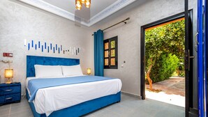 A bedroom with a large bed, a nightstand, a wall-mounted light, and a window with curtains. - Villa Gardens Diafa - 8 rooms (Lahebichate)