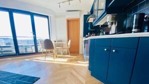 Een moderne keuken met blauwe kastjes, een eethoek met tafel en stoelen, en een groot raam met uitzicht op de stad.