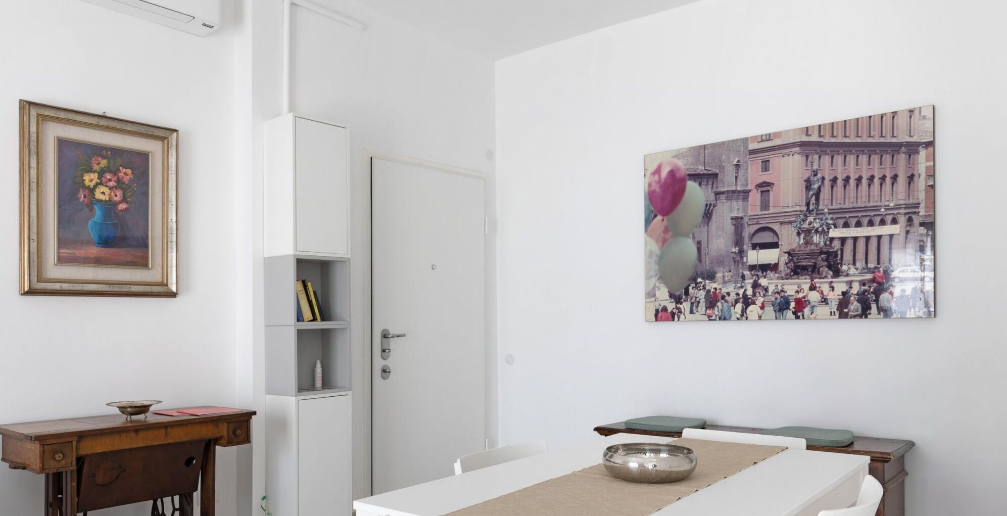 A dining area with a white table, a metal bowl, and a framed painting of flowers.