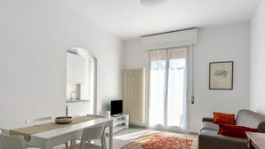 A modern living room with a dining area, a flat-screen TV, and a large window with curtains. - A Casa di Giorgia by Wonderful Italy (Bologna)