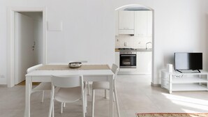 A modern, minimalist kitchen with white cabinetry, a built-in oven, and a dining area with a white table and chairs. - A Casa di Giorgia by Wonderful Italy (Bologna)