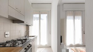 A modern kitchen with a gas stove, a sink, and cabinets. There is a window with curtains and a view of the outside. - A Casa di Giorgia by Wonderful Italy (Bologna)