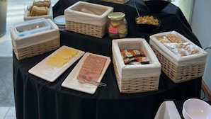 A buffet table with various food items and containers, set against a backdrop of a city street and trees. - Hotel Inizio (San Francisco)