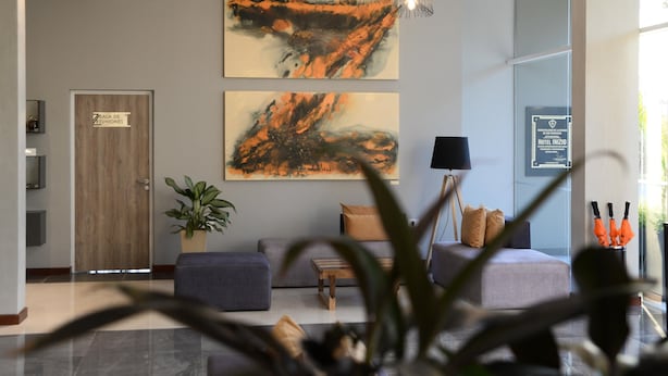 A modern lobby with a wooden door, a seating area with a sofa and ottoman, a potted plant, and two abstract paintings on the wall. - Hotel Inizio (San Francisco)
