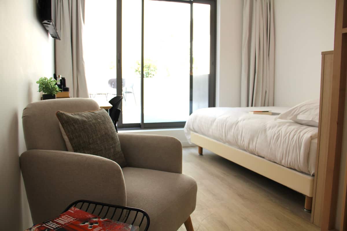 Un dormitorio moderno con cama, una silla y una ventana.