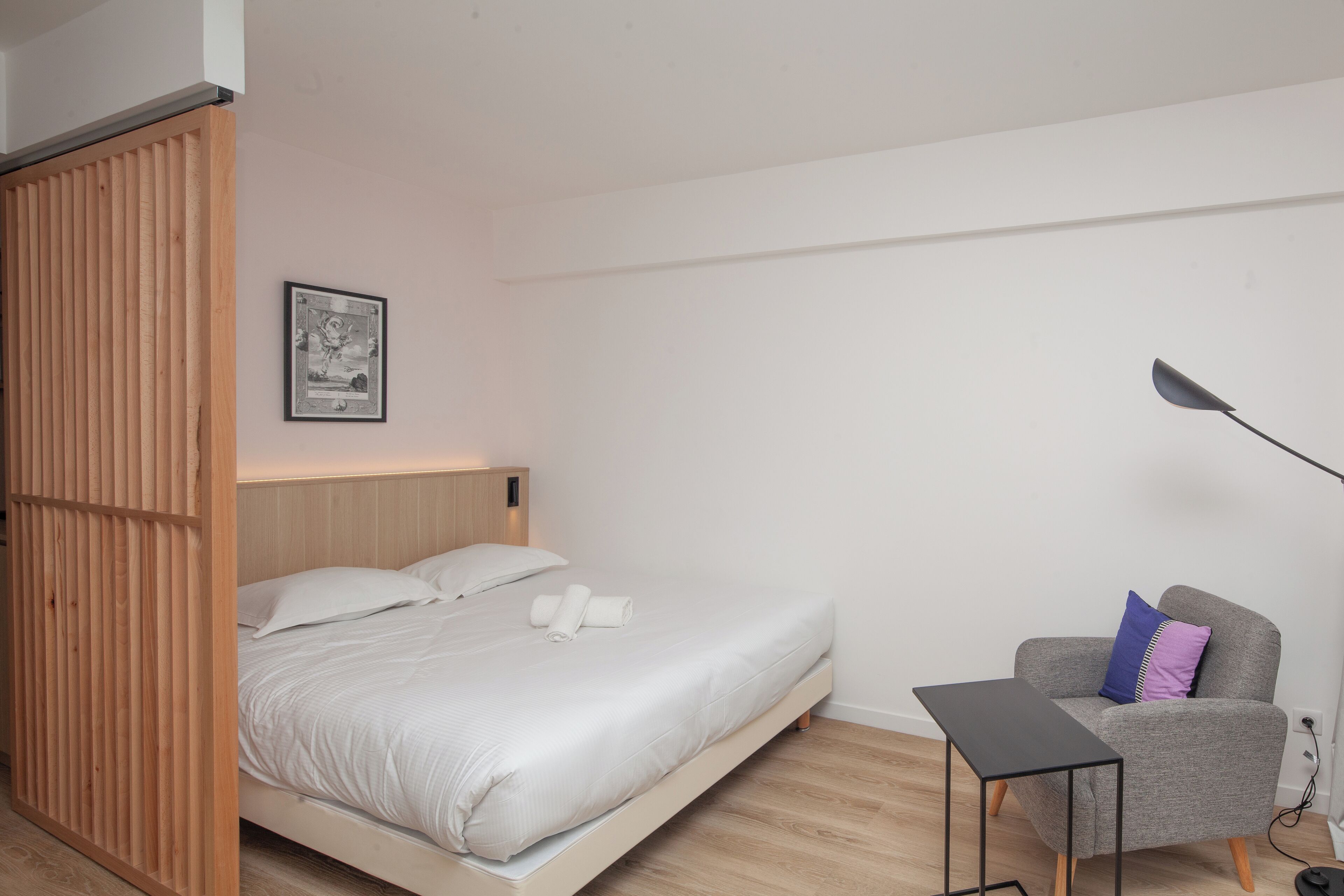 Una camera da letto moderna con un letto, un tavolino, una sedia e una lampada da terra.