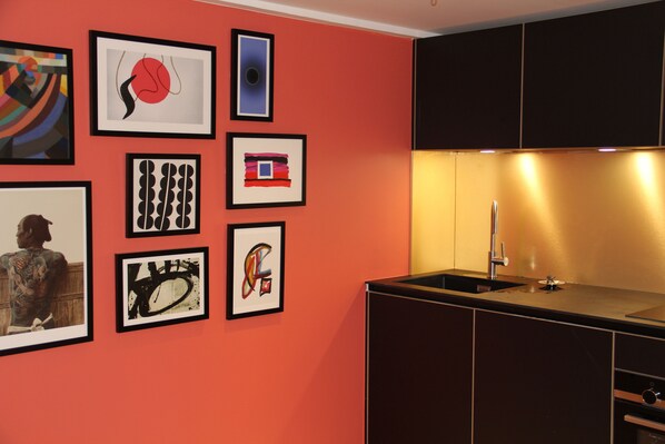 Uma cozinha moderna com bancada preta, pia e parede decorada com diversas obras de arte emolduradas.