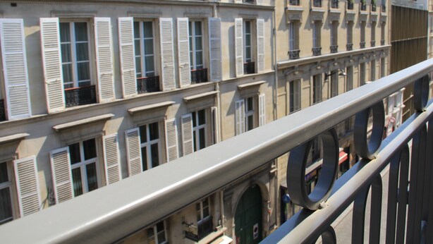 Une rangée d’immeubles au style architectural uniforme, caractérisée par de nombreuses fenêtres avec volets, des balcons et une rambarde métallique au premier plan.