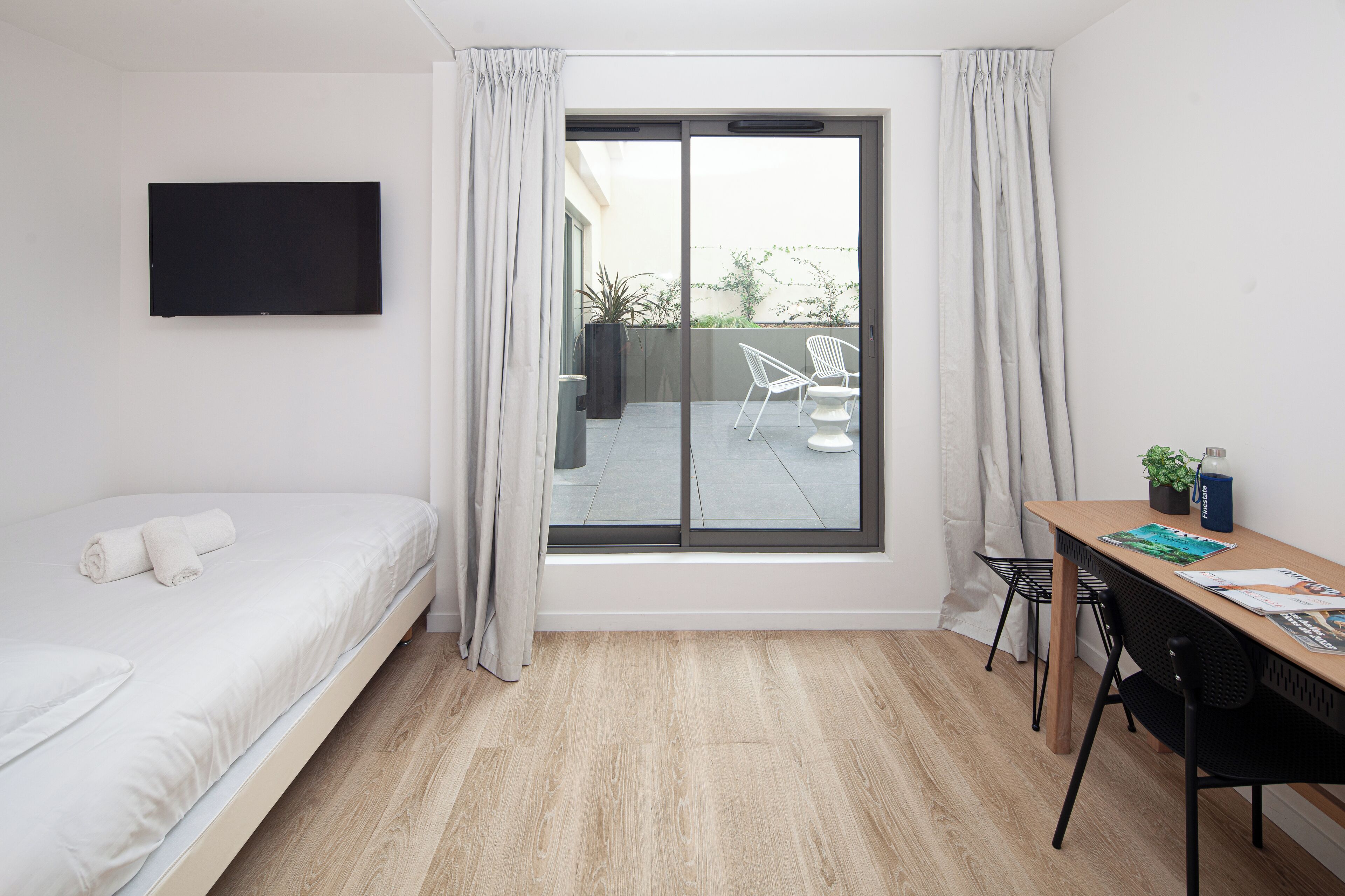Een moderne hotelkamer met een bed, bureau en een groot raam met gordijnen.