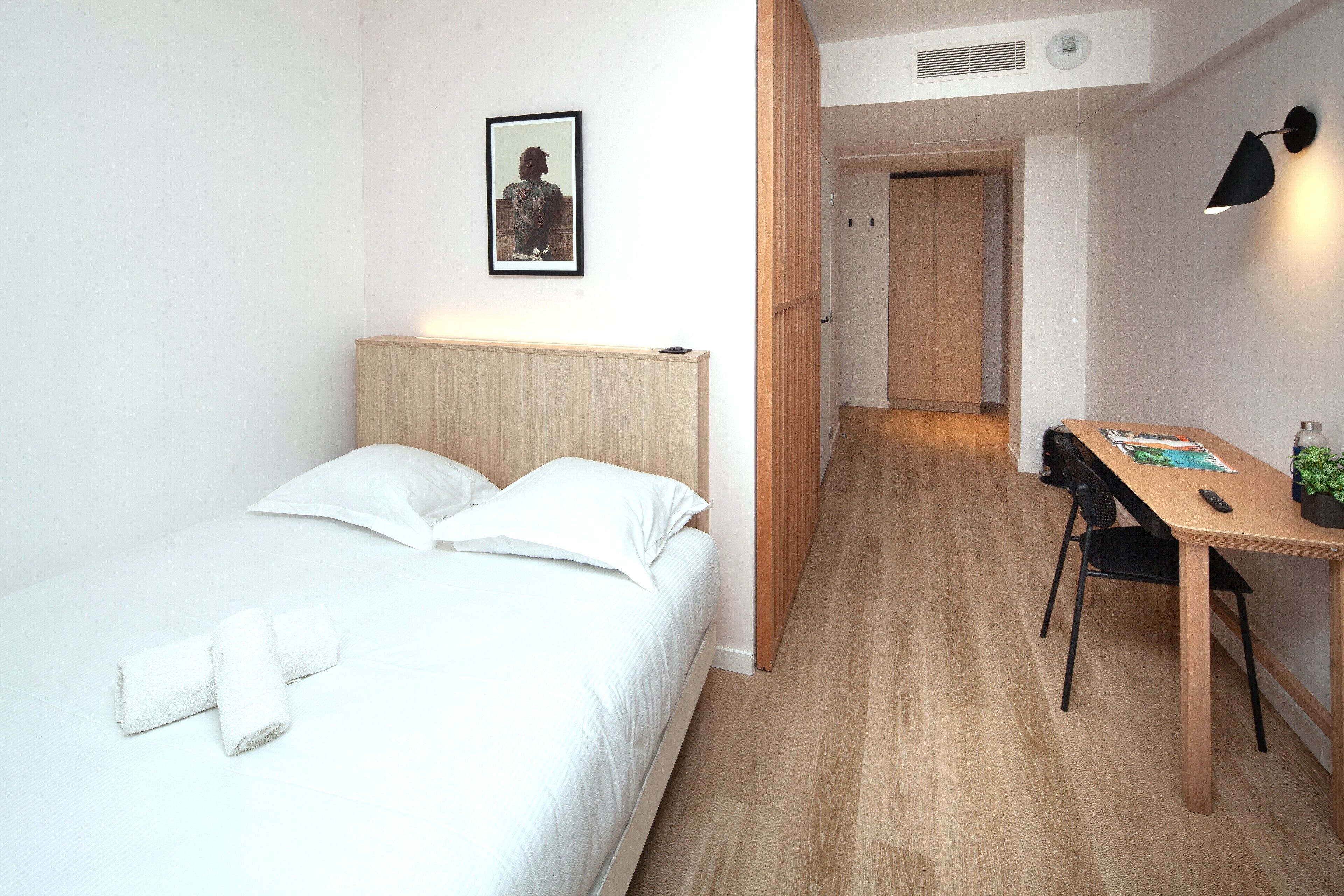 A modern hotel room with a neatly made bed, a desk with a chair, and a framed picture on the wall.