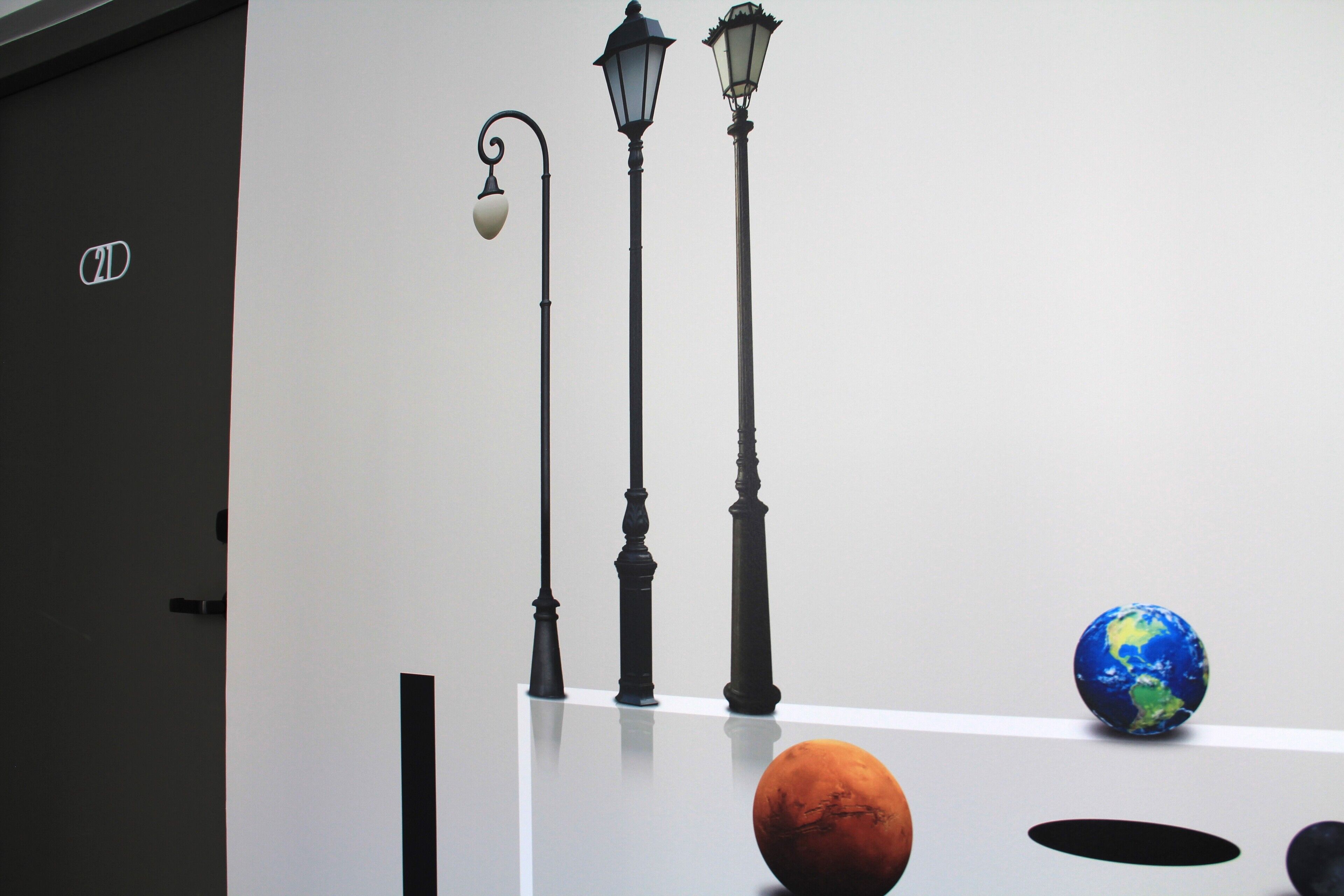 A room with a white wall, a door with a sign, and three black street lamps.