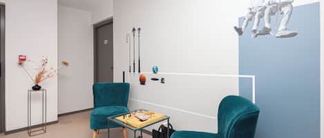 A modern waiting area with teal chairs, a small table with a chessboard, and a wall with a minimalist art piece.