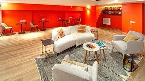 Un salon moderne avec un canapé blanc, des fauteuils gris et une table basse. On y trouve également de petites tables et des chaises, une bibliothèque et un radiateur.