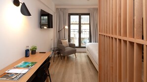 Une chambre à coucher de taille modeste, avec un lit en bois, un bureau et une chaise, une petite table avec une plante et un téléviseur fixé au mur.