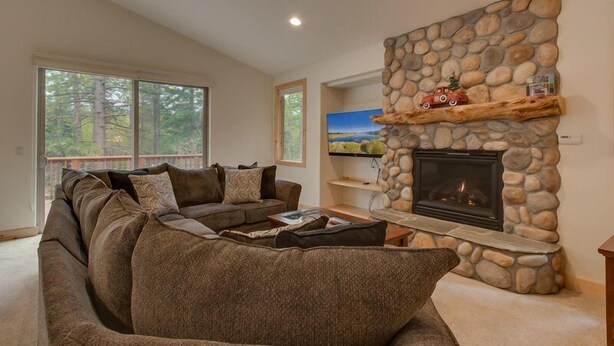 A living room with a stone fireplace, a sectional sofa, and a television on a stone shelf.
