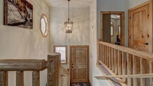 A wooden staircase with a railing leading to a door, a hanging light fixture, and a framed picture on the wall.