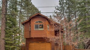 A two-story wooden house with a garage, surrounded by tall trees.