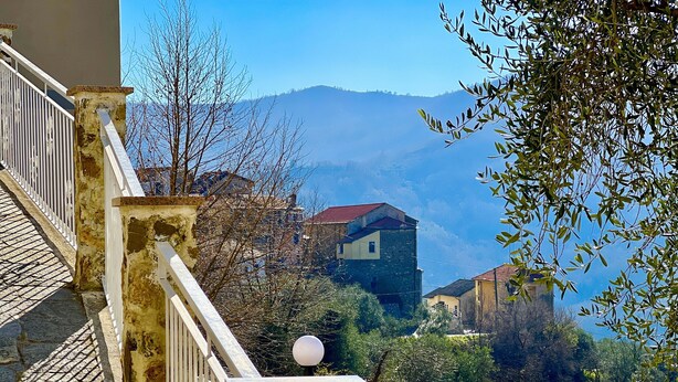 A balcony with a stone balustrade, a view of a mountainous landscape, and a building with a red roof. - Vacation Home Paola Aurigo, relaxation, quiet and 16 km from the sea (Aurigo)
