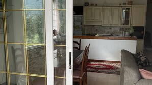 A dining area with a table and chairs, a kitchen in the background, and a sliding glass door leading outside. - Vacation Home Paola Aurigo, relaxation, quiet and 16 km from the sea (Aurigo)
