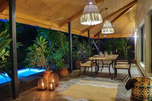 An outdoor dining area with a pool, potted plants, and hanging lights.