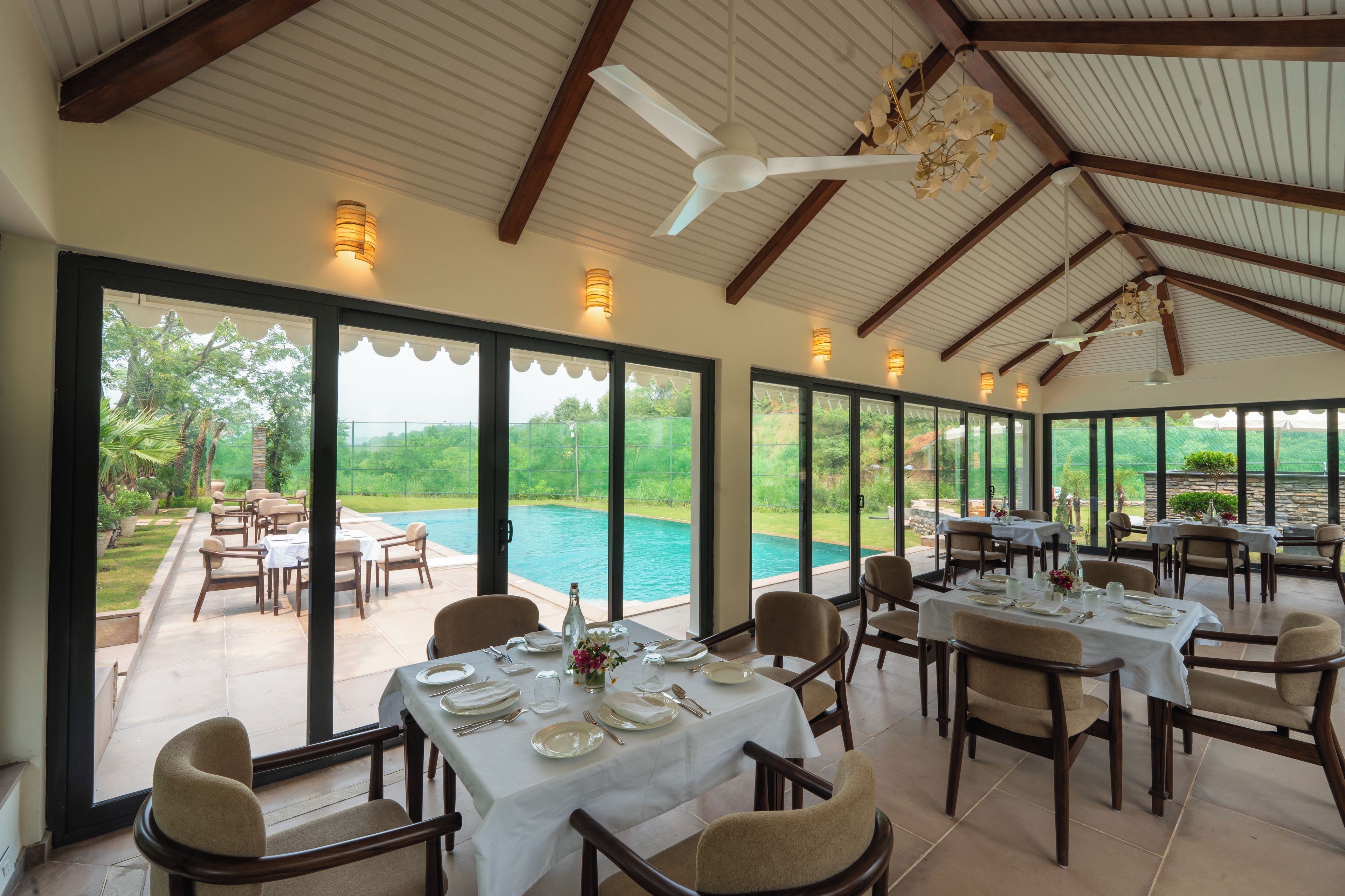 A dining area with tables set for service, overlooking a swimming pool.
