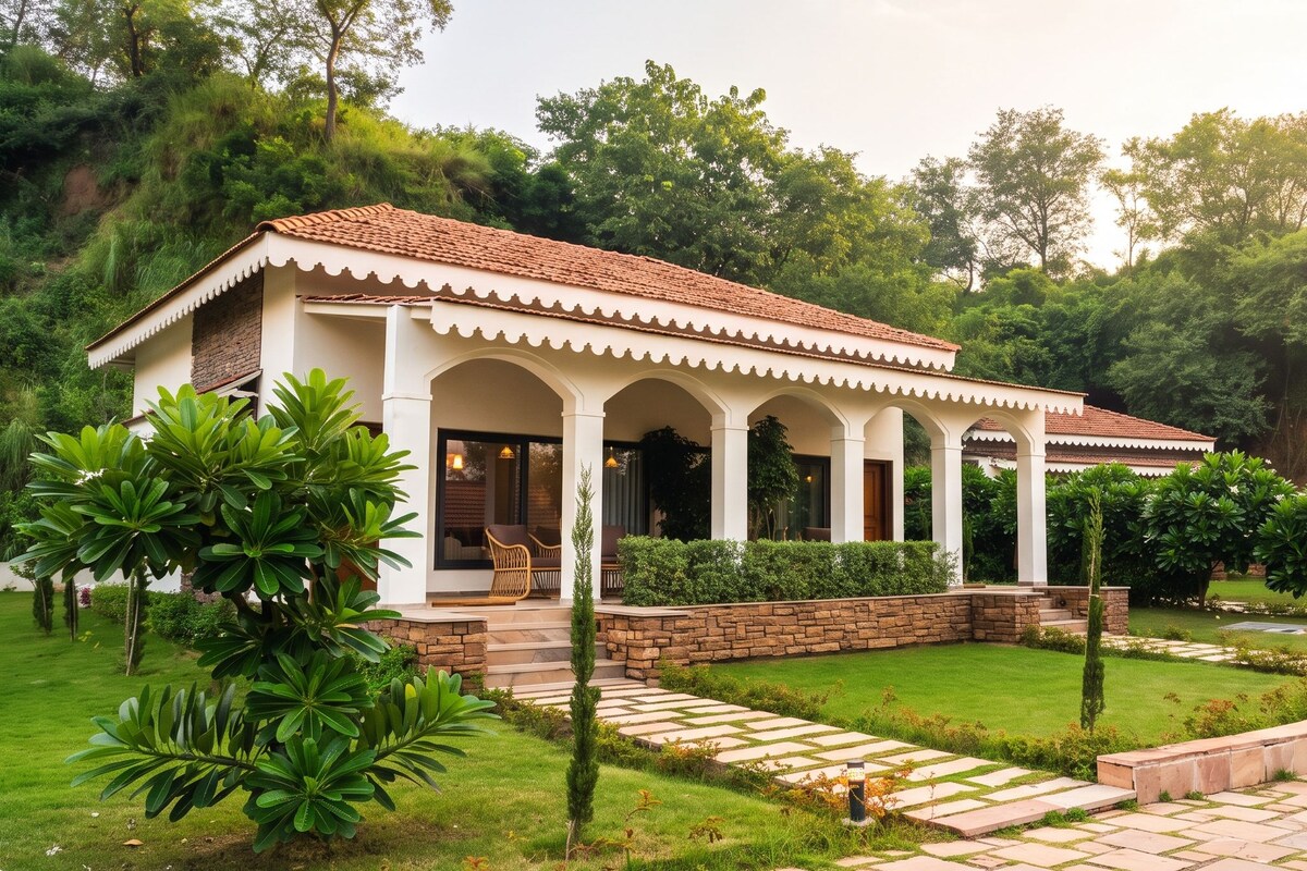 Une maison à deux étages, avec un toit en tuiles, un porche couvert avec des colonnes et un jardin bien entretenu agrémenté d’un chemin en pierre.