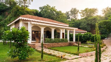 Una casa de dos pisos con techo de tejas, un porche cubierto con columnas y un jardín bien cuidado con un camino de piedra.