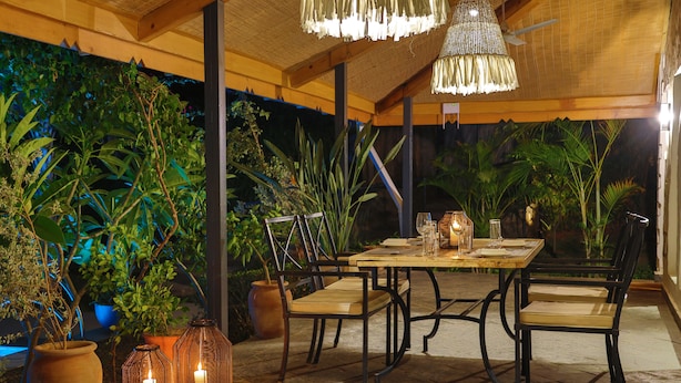Een terras met een tafel en stoelen, omringd door plantenpotten en kaarsen.